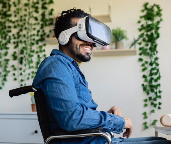 A man in a wheelchair smiling with a VR headset on